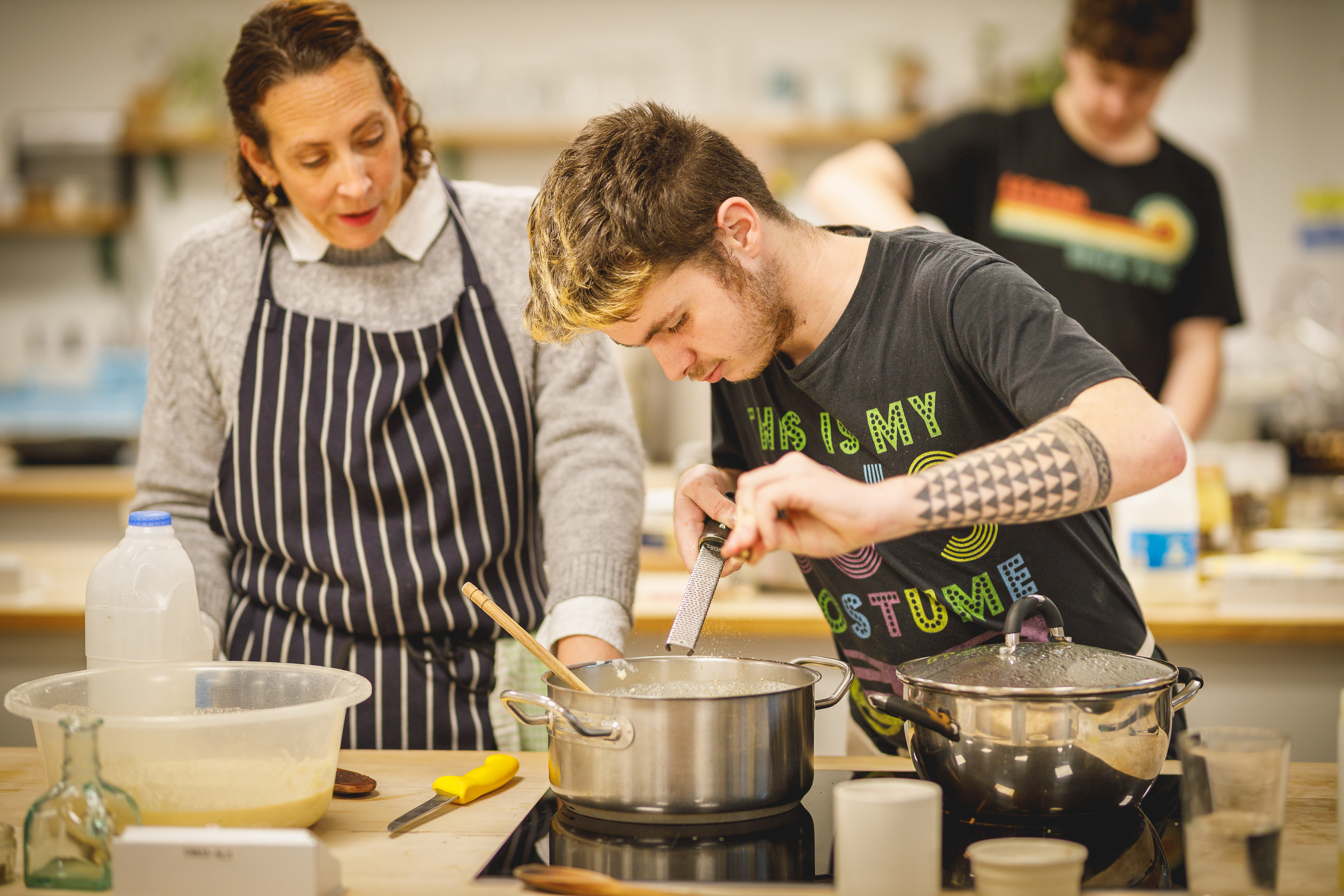 How to be a chef student grating into silver pan with teacher looking.jpg